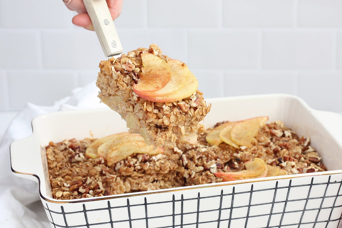 Apple cinnamon baked oatmeal in a white and black checked porcelain dish with a spatula lifting out a slice.