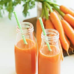 fresh carrot juice with carrots in the background
