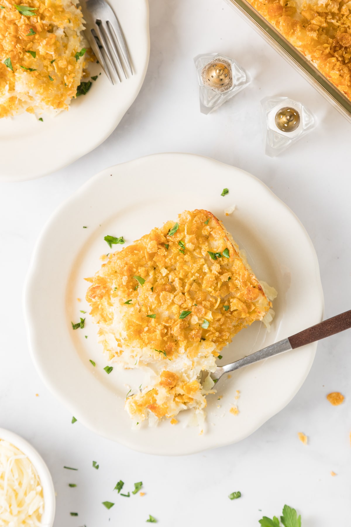 An overhead shot of cheesy potatoes on a white serving plate with a fork.
