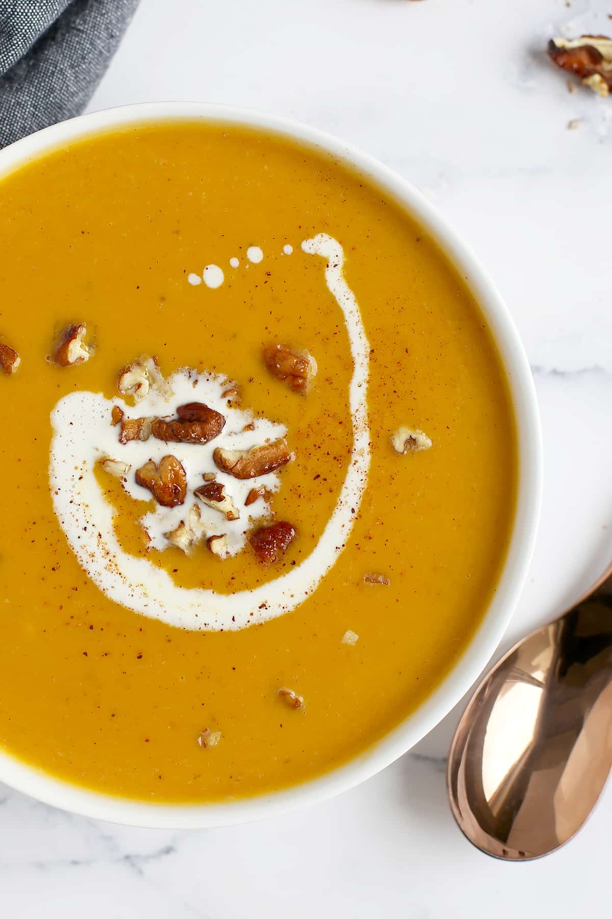 A close up image of creamy butternut squash soup topped with a swirl of cream and crushed maple coated pecans.
