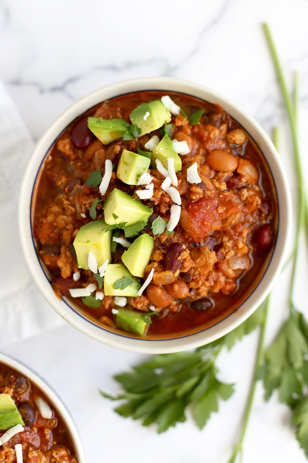 Healthy turkey chili in a small serving bowl topped with chopped avocado and shredded cheese.