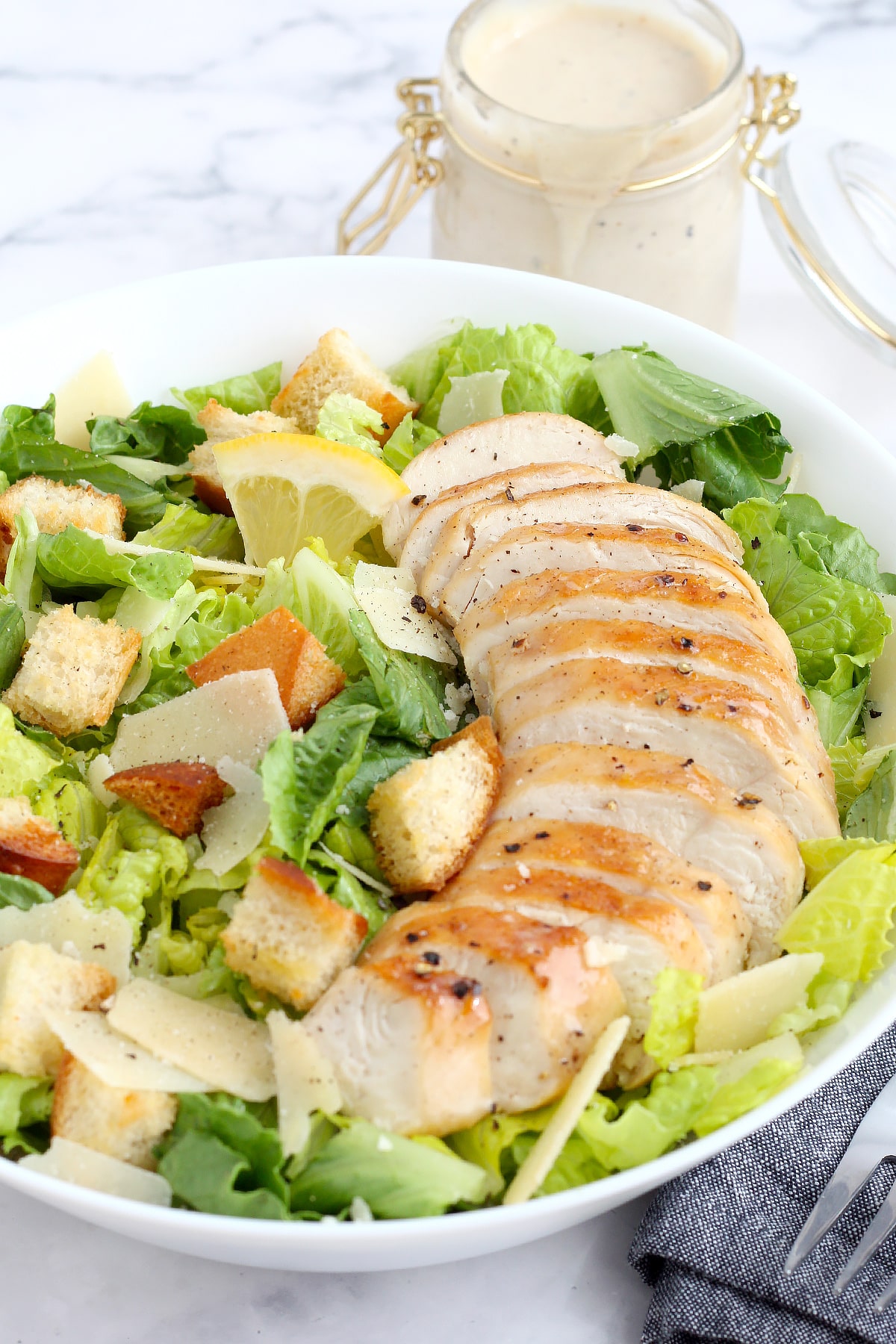 Homemade chicken caesar salad in a white serving bowl with a bottle of dressing in the background.