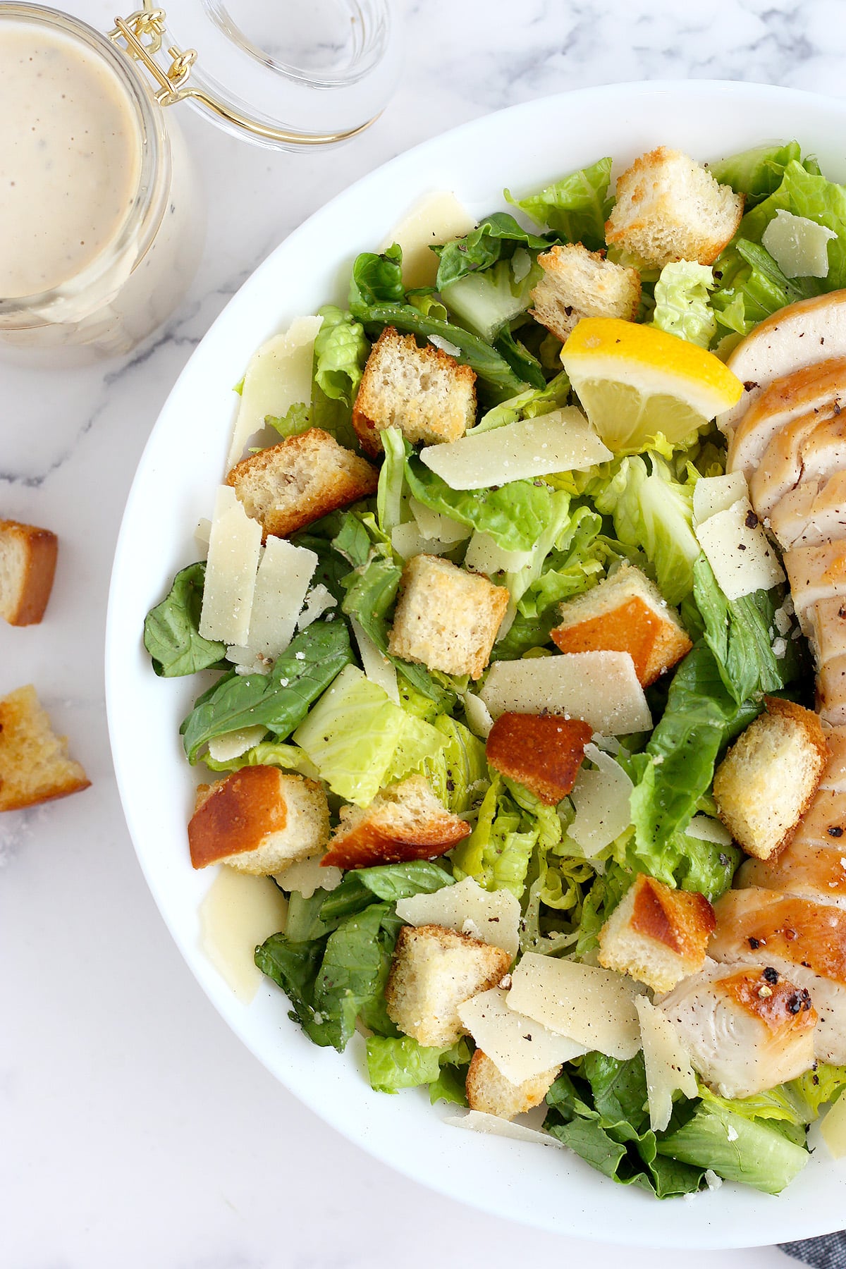 A close up photo of chicken caesar salad with homemade croutons and shaved parmesan cheese.